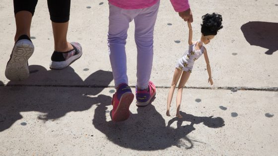 A 4-year-old girl carries a doll while walking with her immigrant mother.