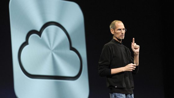 Steve Jobs, in black turtleneck and light jeans, standing in front of a large iCloud logo, seemingly embossed in metal.