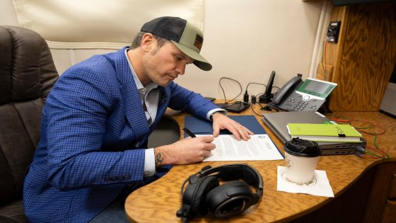 Defense Secretary Pete Hegseth signs a memorandum at a desk aboard an aircraft.