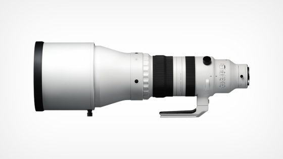 A large white telephoto camera lens with a black front edge and various controls and rings for adjustments on the body, displayed in a side profile against a plain white background.