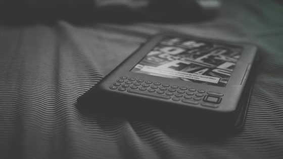 A black and white image of a dark framed e-reader with a keyboard below its e-ink screen. It is on a piece of cloth.