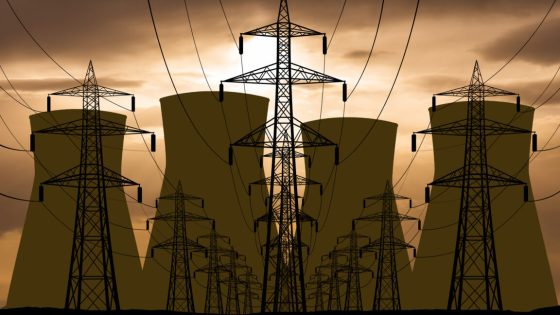 An orange, cloudy sky backlights a set of electrical wires on large pylons, leading away from the cooling towers of a nuclear power plant.
