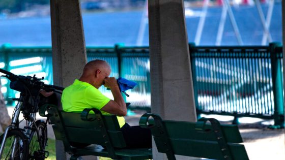 A man wipes his face while sitting on a bench along Memorial Drive in Cambridge in the 90-degree heat Monday. (Jesse Costa/WBUR)