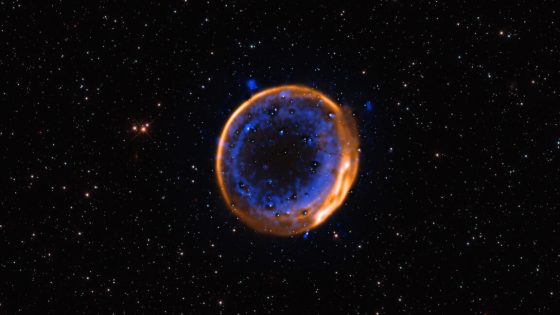Image of a dark background punctuated with stars, with a bright ring in the center that is comprised of an outer orange and inner blue ring.