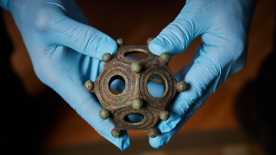 A person with blue latex gloves holds a 12-sided bronze object