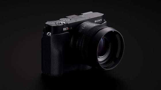 A black Sony RX1R II digital camera with a large lens is shown angled slightly to the right against a dark background.